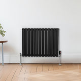 Schwarzer ovaler Röhrenheizkörper mit Chrom-Thermostatventilen, 600mm x 780mm, an einer hellen Wand, Holzfußboden, modern und elegant