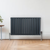Ovaler Röhrenheizkörper in Anthrazitgrau, 600mm x 1020mm, mit Chrom-Thermostatventilen, modernes Design und glatte, matte Oberfläche auf einem hellen Holzboden