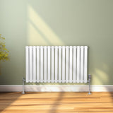 Ovaler Röhrenheizkörper in Weiß mit Chrom-Thermostatventilen, 600mm x 1020mm, elegant an einer hellgrünen Wand, Holzfußboden und sanftem Licht