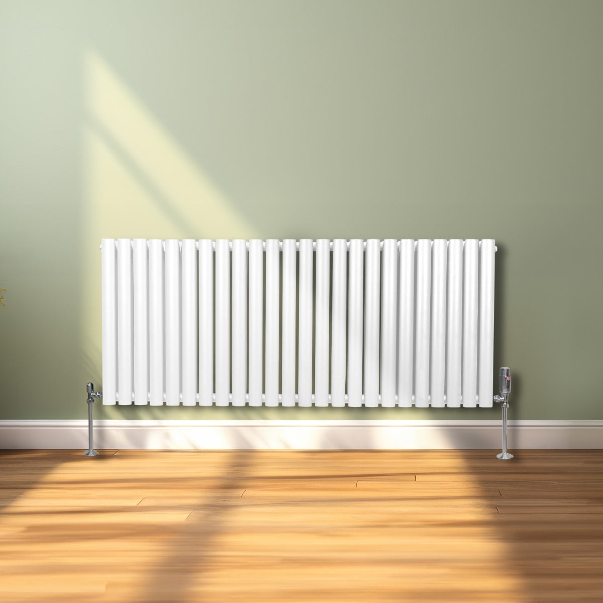 Ovaler Röhrenheizkörper in Weiß, 600mm x 1440mm, mit glänzenden Chrom-Thermostatventilen, vor einer hellgrünen Wand und Holzfußboden