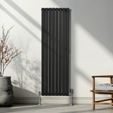 Schwarzer ovaler Röhrenheizkörper mit Chrom-Thermostatventilen, 1600mm x 480mm, an einer hellen Wand, umgeben von minimalistischer Einrichtung