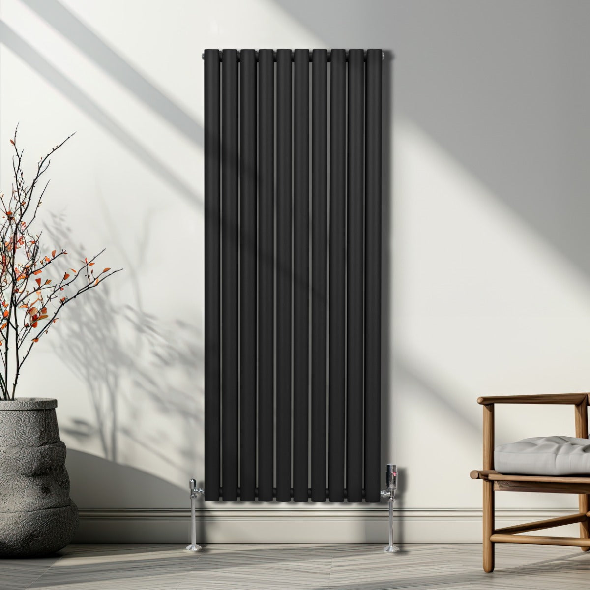 Schwarzer ovaler Röhrenheizkörper mit Chrom-Thermostatventilen, 1600mm x 600mm, an einer hellen Wand, umgeben von minimalistischem Mobiliar und Pflanzen