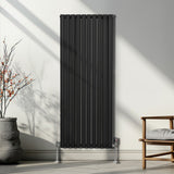 Schwarzer ovaler Röhrenheizkörper mit Chrom-Thermostatventilen, 1600mm x 600mm, an einer hellen Wand, umgeben von minimalistischem Mobiliar und Pflanzen