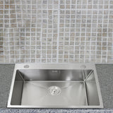 Edelstahl Küchenspüle mit quadratischer Form, glänzender Oberfläche und zentralem Abfluss, vor einer hellen, gefliesten Wand mit Mosaikdesign