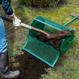 Grüner Garten Kompoststreuer aus Metall, mit grobem Netz, wird mit einer Schaufel gefüllt, während frischer Kompost auf den Boden verteilt wird