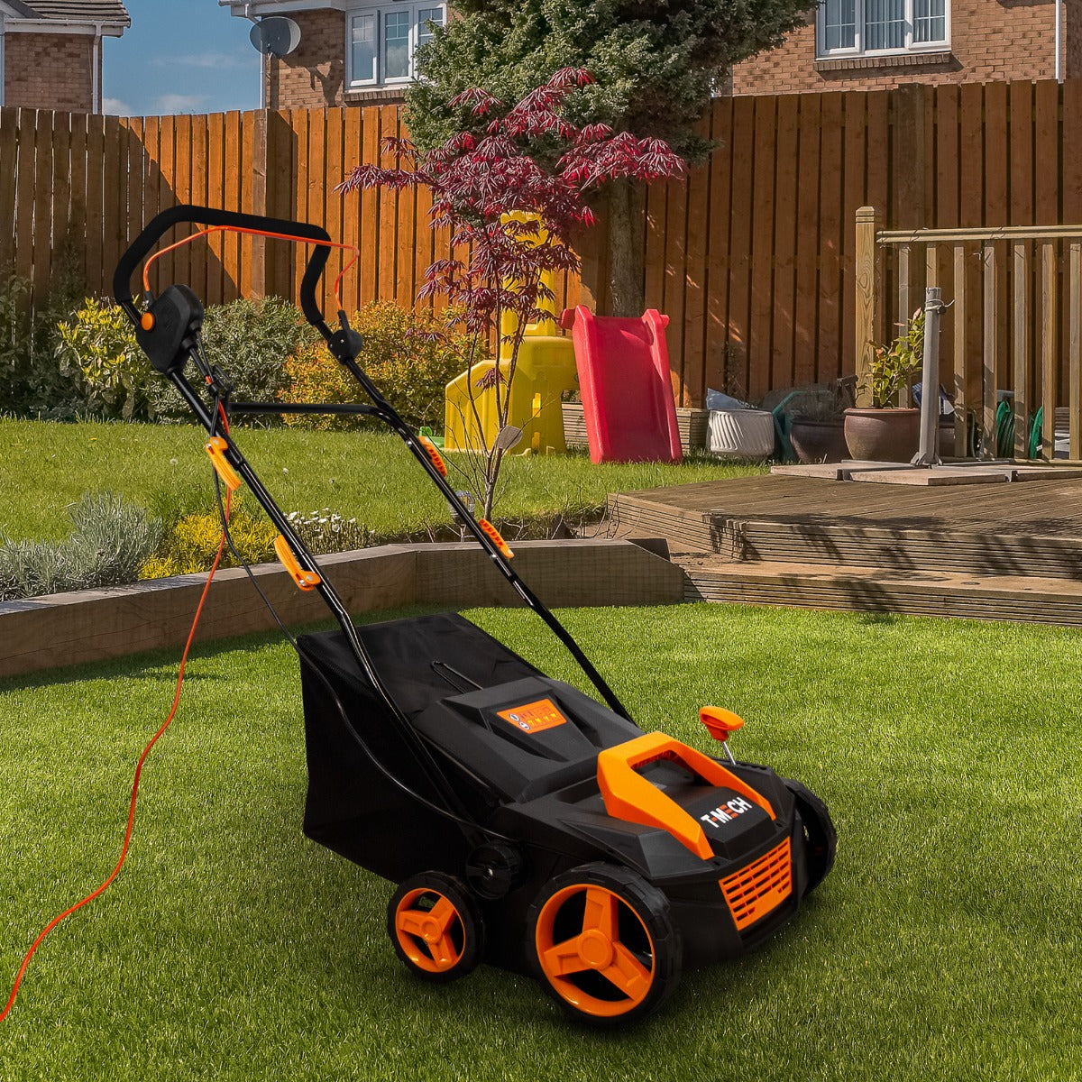 T-Mech Staubsauger für Kunstrasen in Schwarz und Orange, mit robusten Rädern und ergonomischem Griff, auf grünem Rasen im Garten platziert