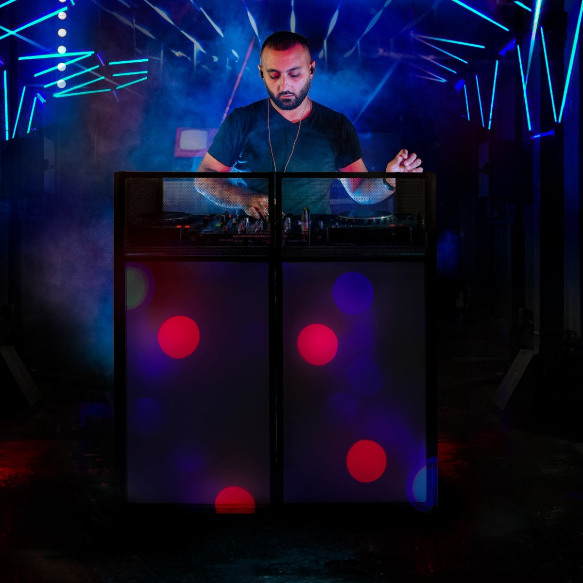 Moderne DJ-Booth-Kabine mit bunten Lichtern, einem DJ in schwarzem Shirt, der an einem Mischpult arbeitet, umgeben von lebhaften Farben und Nebel