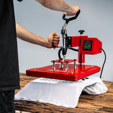Schwenkbare Transferpresse in leuchtendem Rot, bedruckt ein weißes T-Shirt auf einer Holzoberfläche, digitale Temperatur- und Zeitanzeige sichtbar