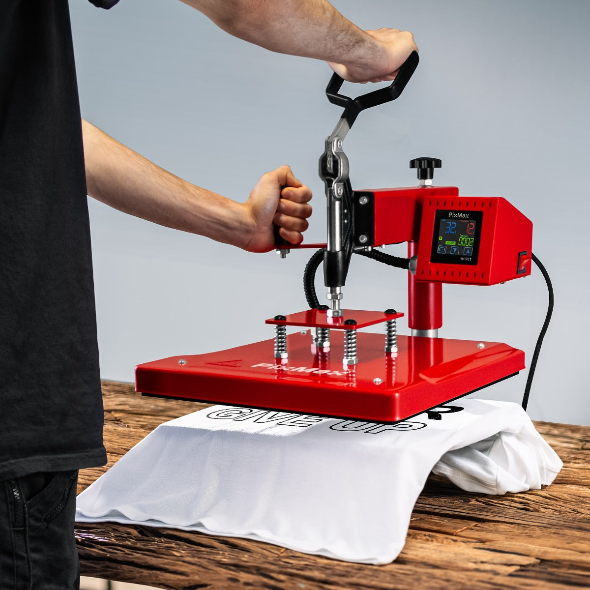 Rote PixMax Schwing Transferpresse mit digitalem Display, die auf ein weißes T-Shirt druckt, auf einer Holzoberfläche platziert