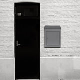 Grauer Anti-Diebstahl Paketkasten aus Metall, rechteckig, an einer weißen Ziegelwand neben einer schwarzen Tür montiert, bietet sicheren Versandschutz