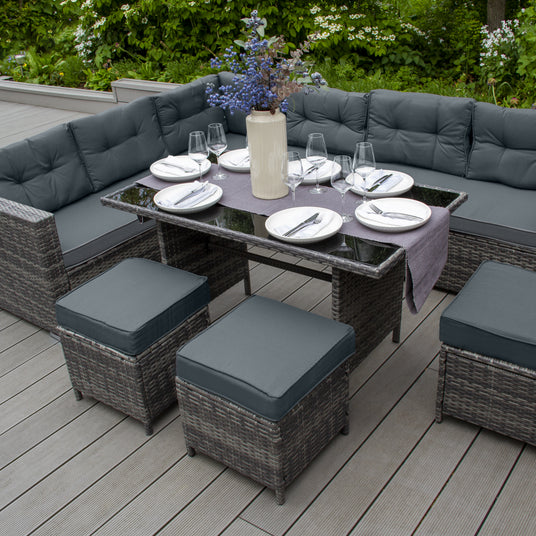 Eleganter Gartenessbereich mit einem runden Tisch, gepolsterten Stühlen in Grau und einer Vase mit bunten Blumen, umgeben von grüner Natur