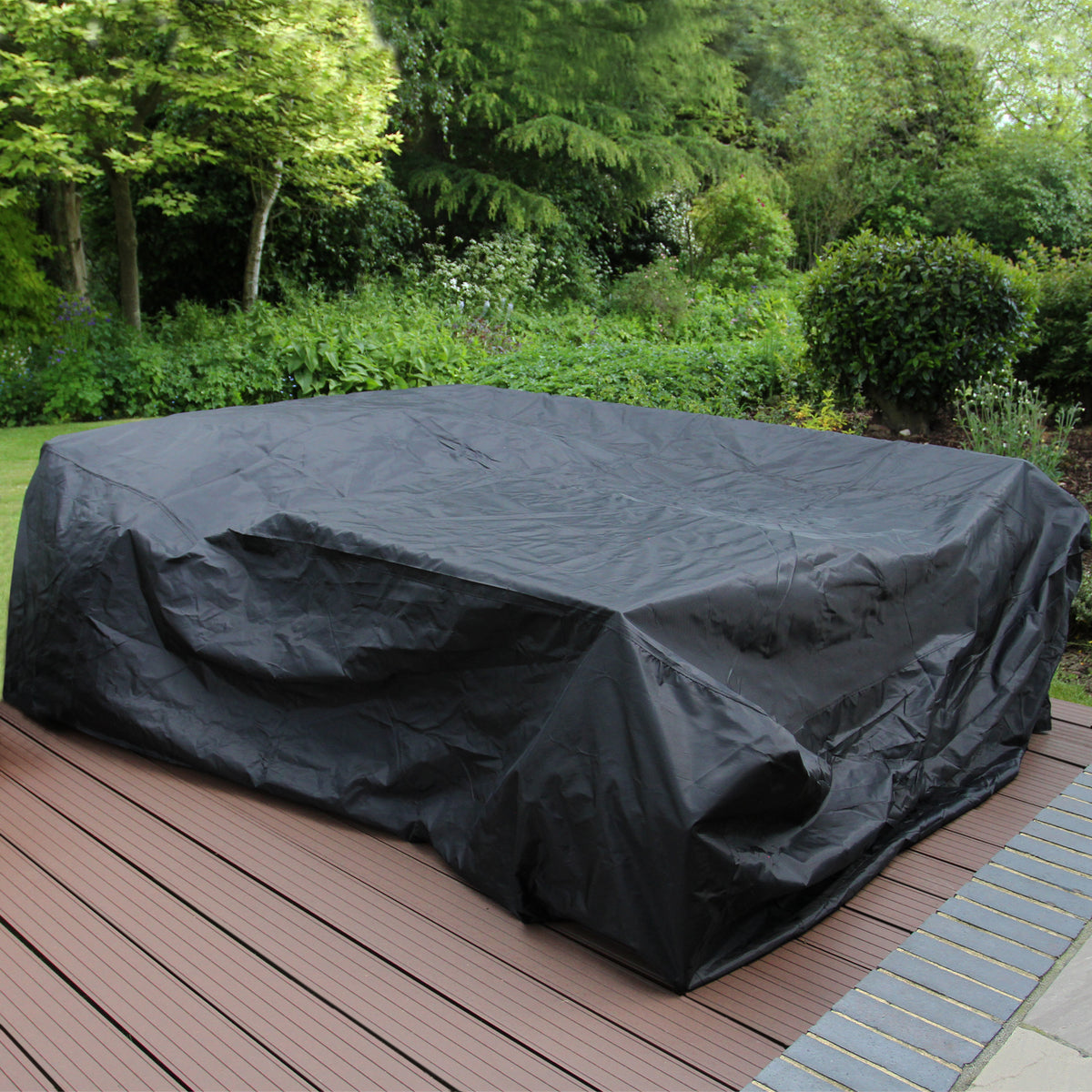 Schwarze Polyrattan Gartenmöbelabdeckung auf einer Holzterrasse, umgeben von üppigem Grün und Bäumen, schützt die Möbel vor Witterungseinflüssen