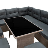 Rattan-Eckset in Grau mit bequemen, gepolsterten Sitzkissen und einem eleganten, schwarzen Glastisch in der Mitte, ideal für den Außenbereich