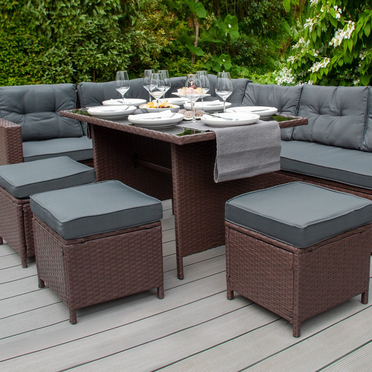 Braunes Polyrattan Gartenmöbel Set mit komfortablen, grauen Sitzkissen, einem eleganten Tisch und stilvollen Hockern, ideal für den Außenbereich