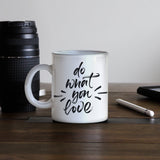 Weißer Becher mit schwarzer Schrift "do what you love", umgeben von einer Kamera und einem Notizbuch auf einem Holztisch