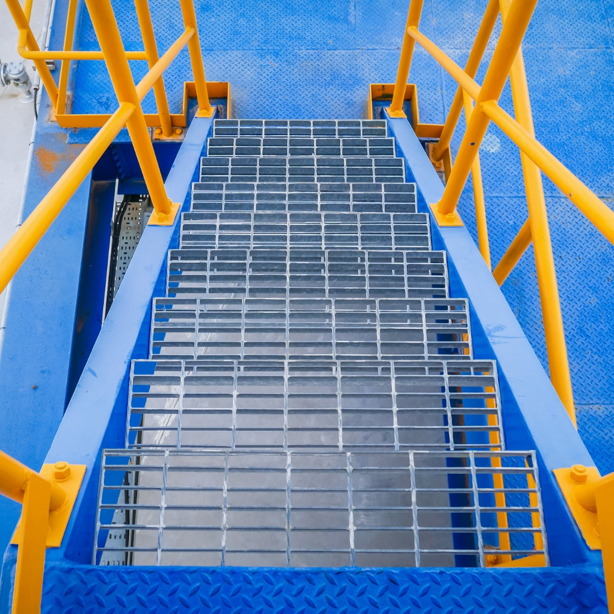 Verzinkte Gitterroste in rechteckiger Form, 800mm x 270mm, mit rutschfester Oberfläche, auf einer blauen Treppe mit gelben Geländern platziert