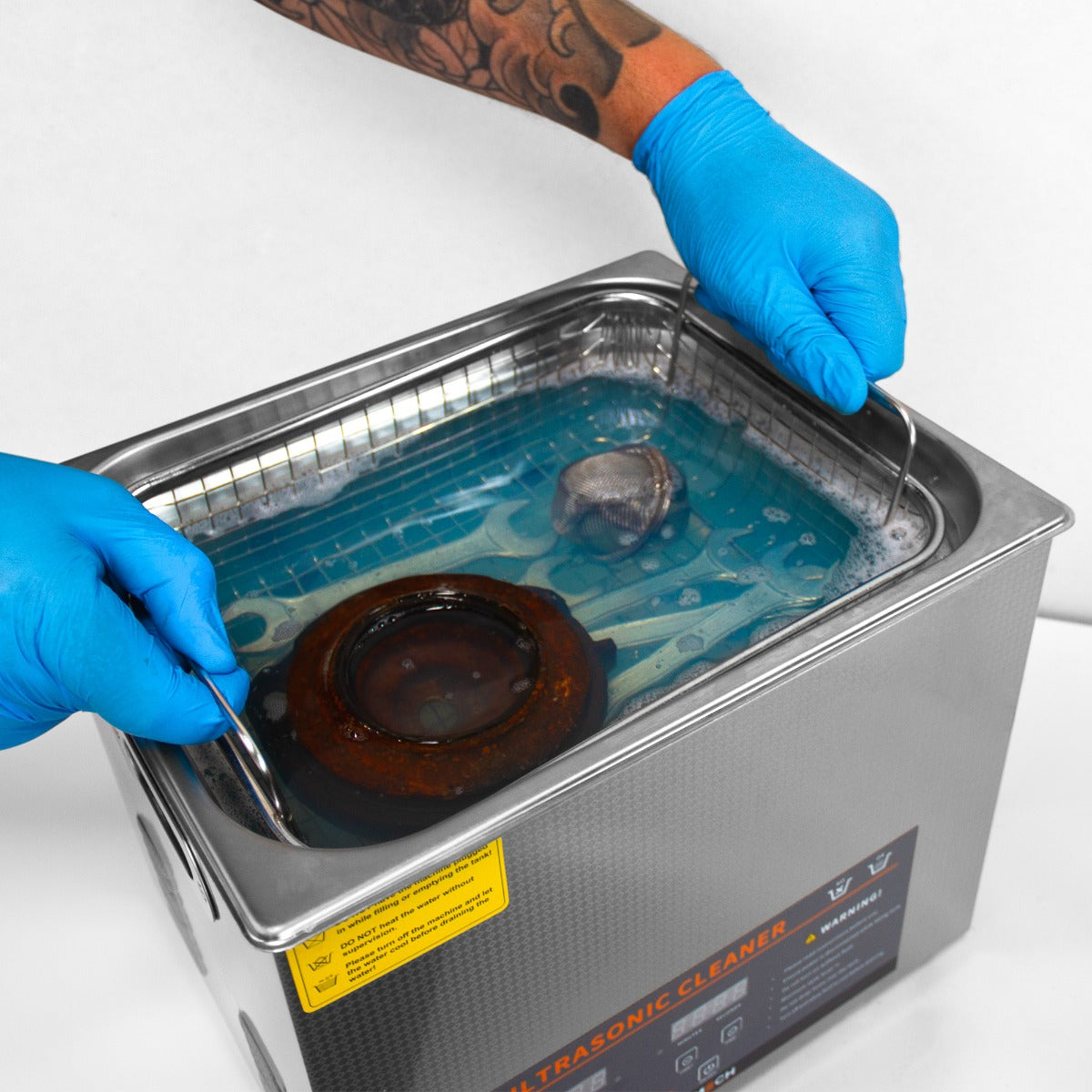 Der T-Mech Ultraschallreiniger mit 10L Kapazität, glänzendes Metallgehäuse, blauer Reinigungslösung und einem Benutzer mit blauen Handschuhen, der ein Teil herausnimmt