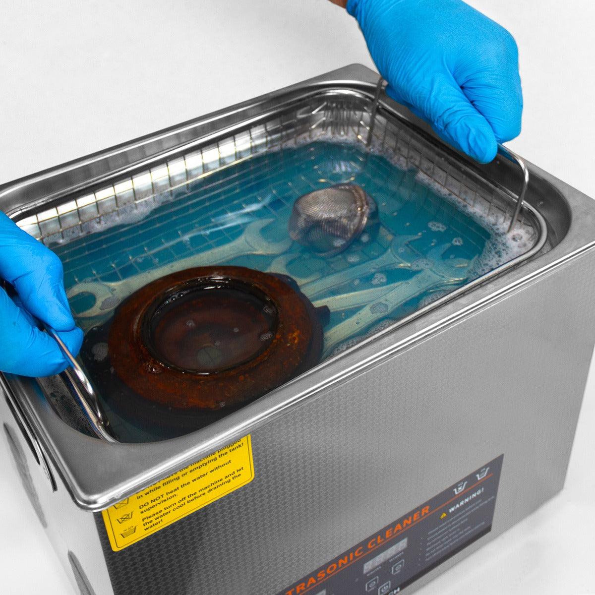 Der T-Mech Ultraschallreiniger mit 30L Edelstahlbehälter, gefüllt mit blauer Reinigungsflüssigkeit, zeigt eine Hand mit blauen Handschuhen, die einen Gegenstand greift
