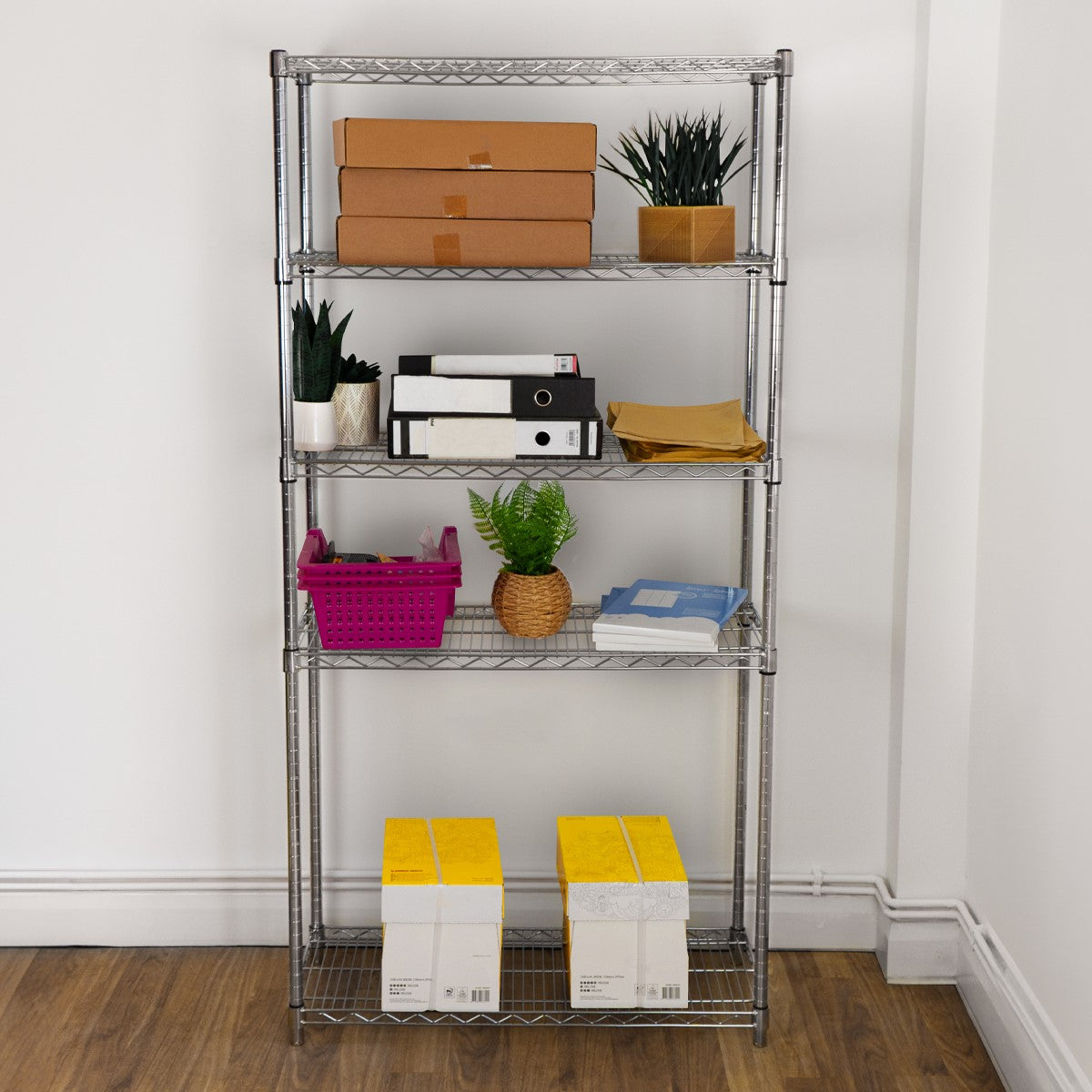 Drahtregal in silber mit fünf Regalböden, gefüllt mit Kisten, Pflanzen und Büromaterialien, auf einem Holzboden in einem hellen Raum