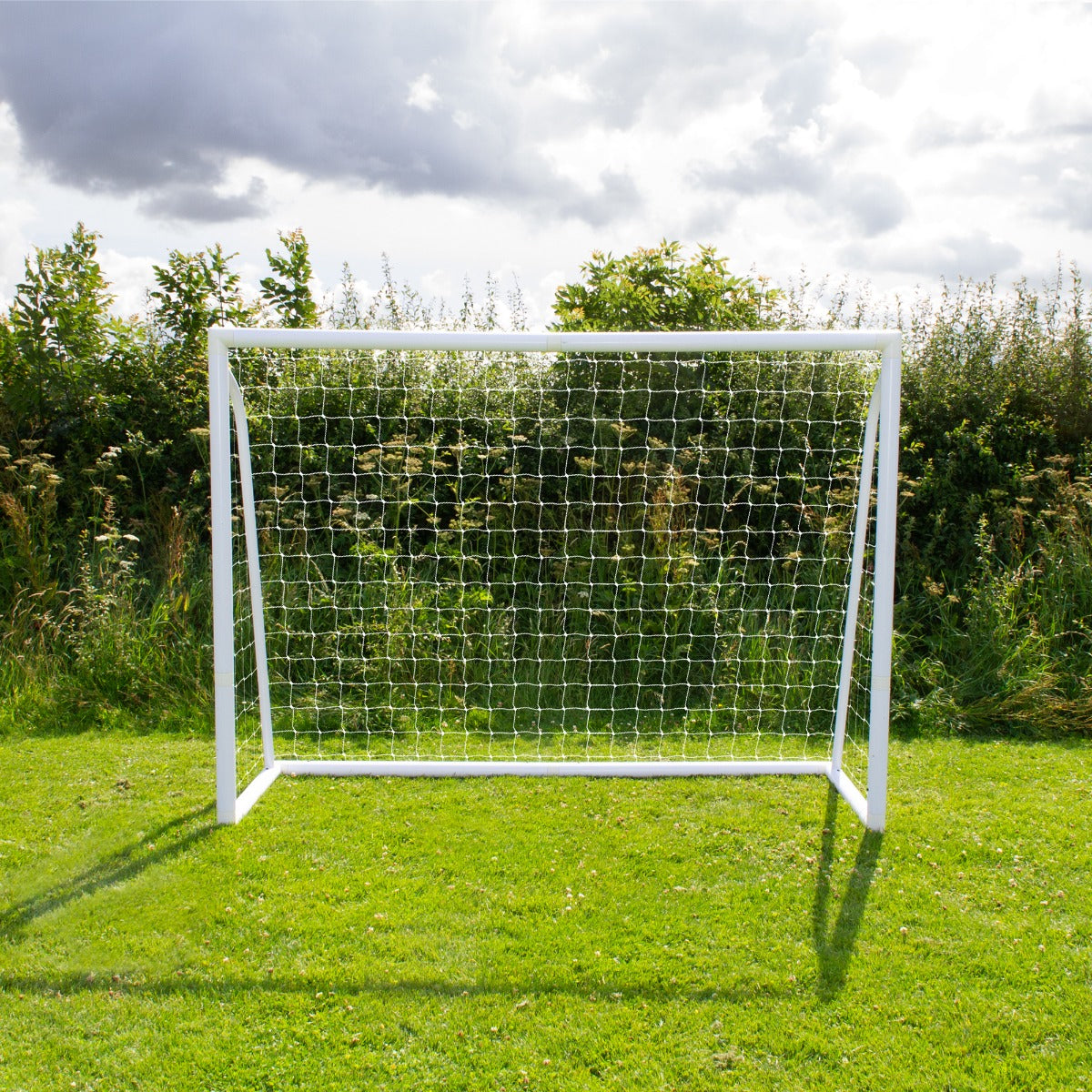 Weißes Fußballtor mit Netz, 2,4m x 1,8m, auf grünem Rasen, umgeben von Bäumen und Gras, ideal für Garten oder Sportplatz, inklusive Tragetasche