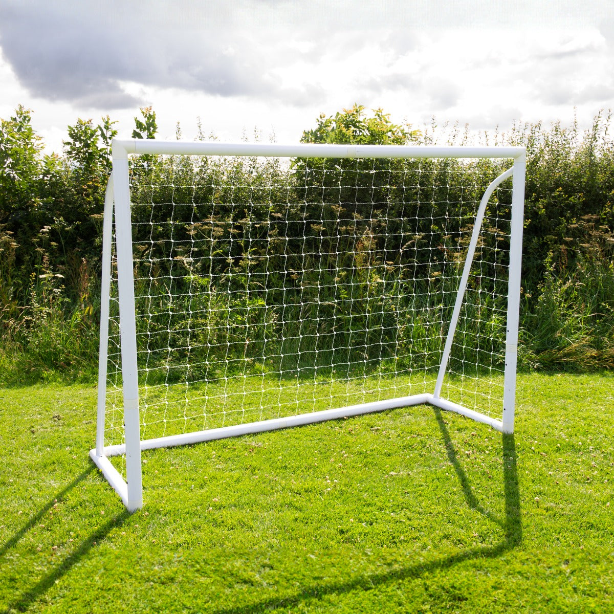 Weißes Fußballtor mit Netz, 2,4m x 1,8m, auf grünem Rasen, umgeben von Bäumen und Sträuchern, ideal für Garten- und Freizeitspiele