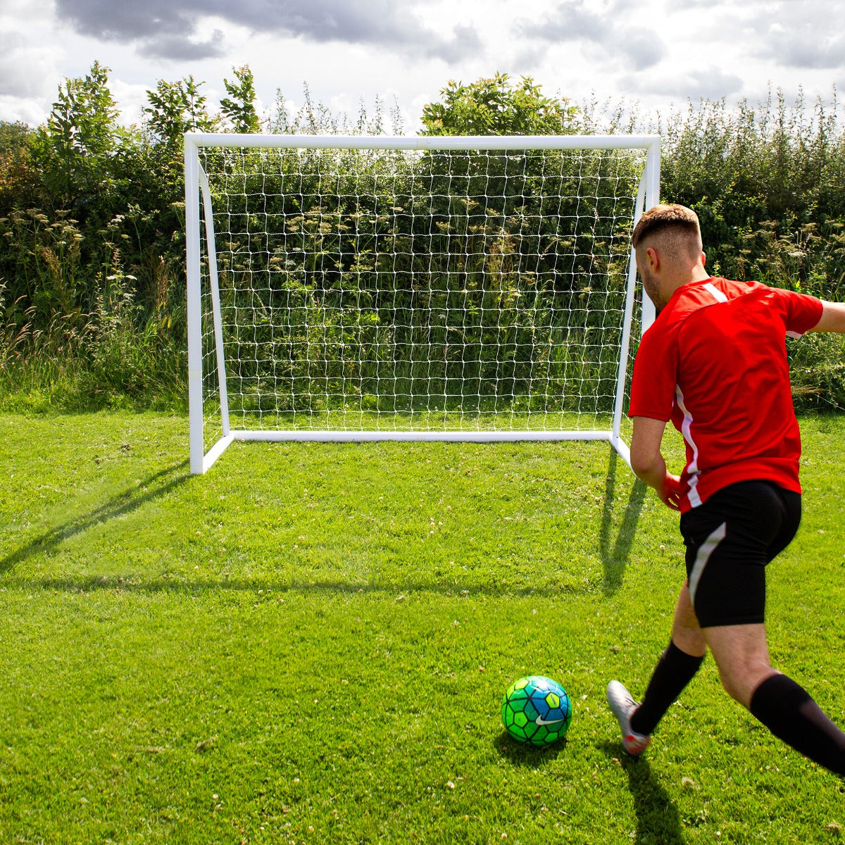 Fußballtor 2,4m x 1,8m aus robustem Kunststoff, auf grünem Rasen, mit einem Spieler in rotem Trikot, der einen bunten Fußball schießt