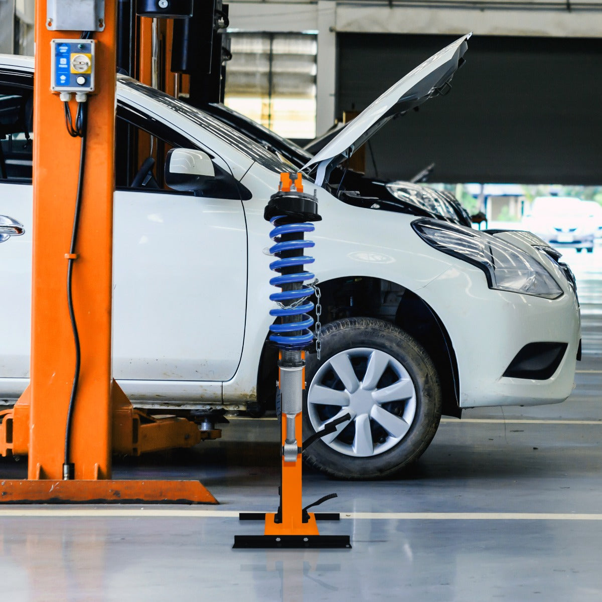 Hydraulischer Federbein-Kompressor in leuchtendem Orange mit blauer Feder, neben einem weißen Auto in einer Werkstatt, ideal für die Fahrzeugwartung