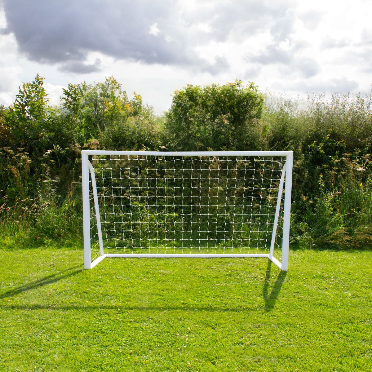 Weißes Fußballtor mit Netz, 1,8m x 1,2m, auf grünem Rasen, umgeben von Bäumen und Sträuchern, ideal für Garten oder Sportplatz