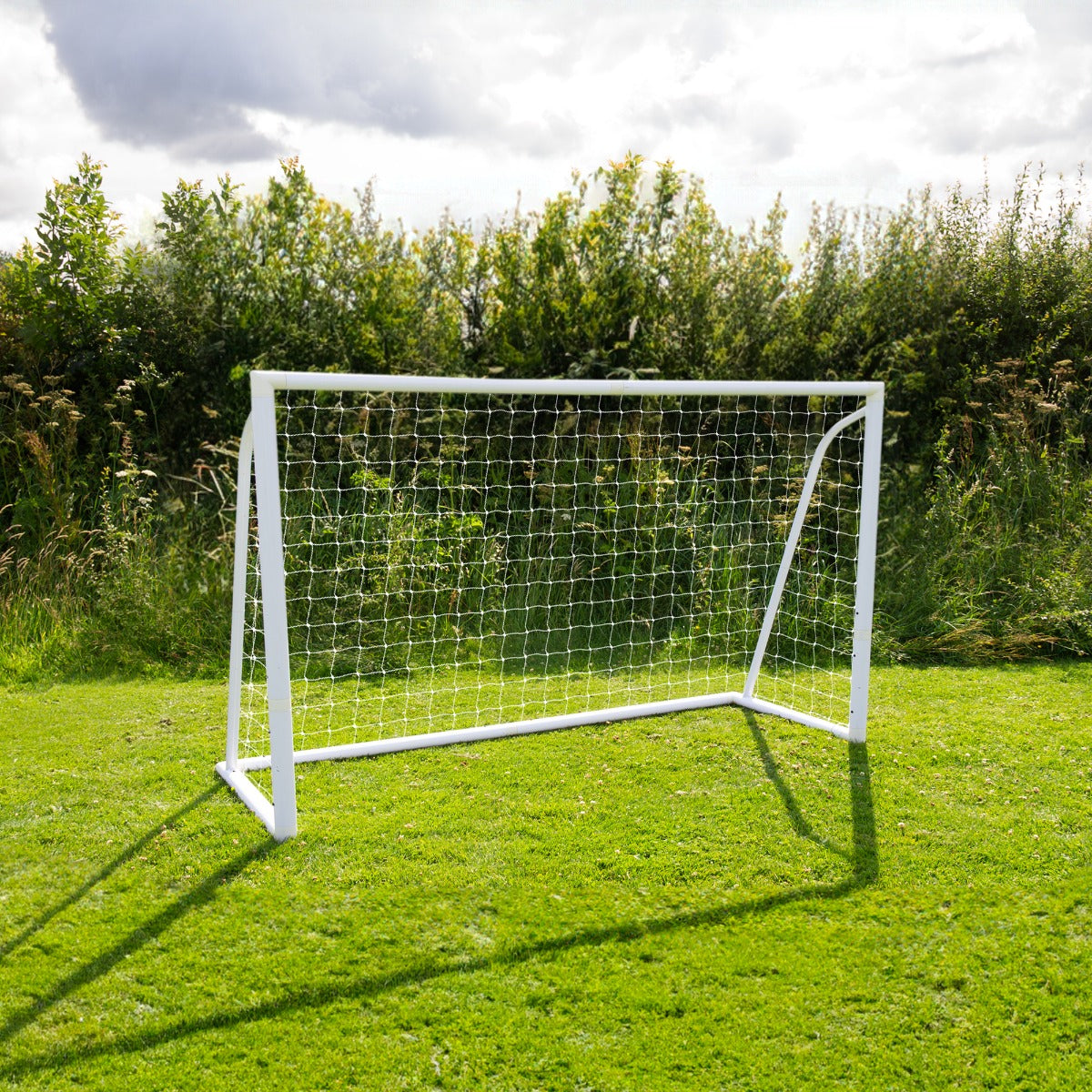 Weißes Fußballtor mit Netz auf grünem Rasen, umgeben von Bäumen und Sträuchern, ideal für Garten- oder Freizeitspiele
