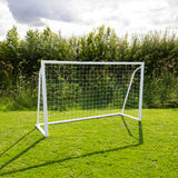 Weißes Fußballtor mit Netz auf grünem Rasen, umgeben von Bäumen und Sträuchern, ideal für Garten- oder Freizeitspiele