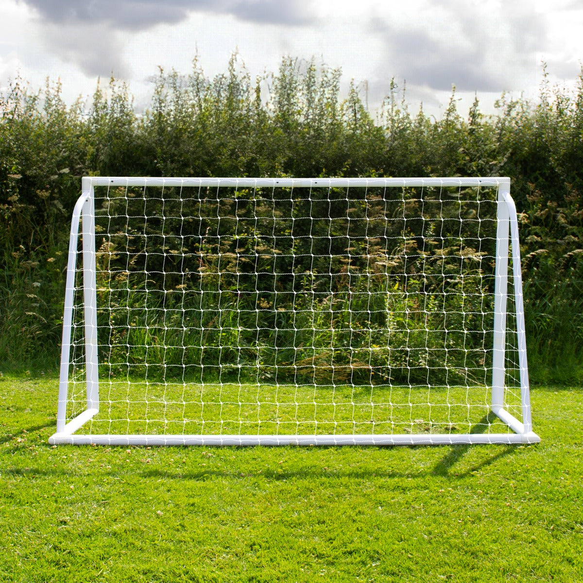 Weißes Fußballtor mit Netz, 1,8m x 1,2m, auf grünem Rasen, umgeben von Bäumen und einem bewölkten Himmel, ideal für Garten- oder Freizeitspiele