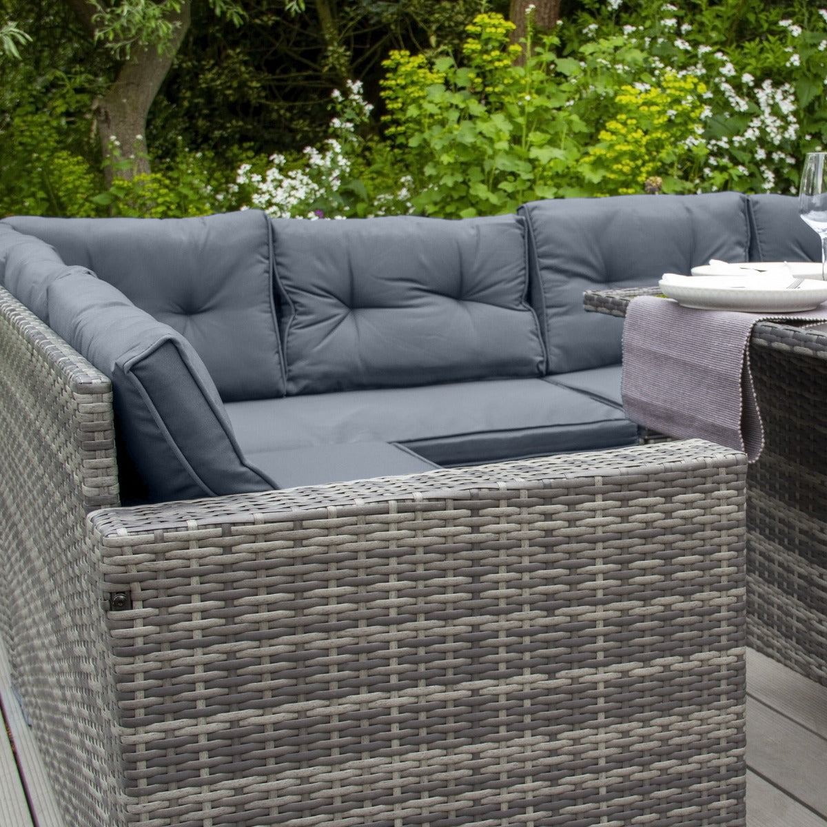 Polyrattan Gartenmöbel Set in Grau mit bequemen, gepolsterten Kissen, ideal für den Außenbereich, umgeben von üppigem Grün und Blumen