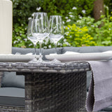 Elegantes Polyrattan Gartenmöbel Set in Grau mit einem Tisch, Gläsern und Geschirr, umgeben von üppigem Grün und blühenden Pflanzen