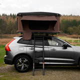 Braunes Auto Dachzelt auf einem grauen SUV, mit einer stabilen Leiter, ideal für Camping und Outdoor-Abenteuer in der Natur