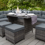 Grau Rattan Eckgarnitur mit bequemen Kissen, eleganter Glastisch, stilvolle Gläser und eine Flasche Sekt, umgeben von grünem Gartenambiente
