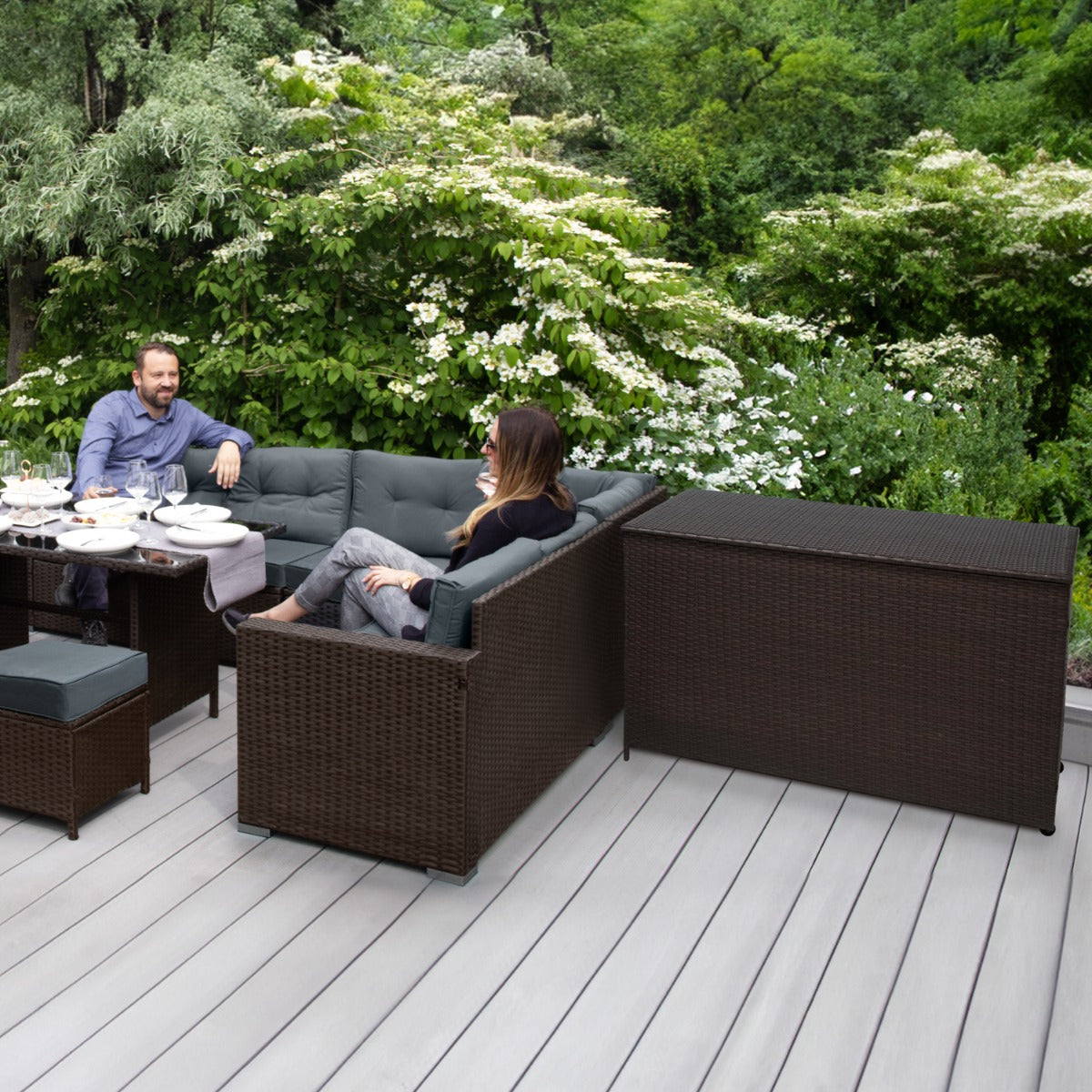 Braune Rattan Eckgarnitur mit bequemen Kissen, umgeben von grüner Natur, ideal für entspannte Stunden im Freien, inklusive Kissenbox
