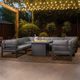 Modulares Gartenlounge-Set in Grau mit integrierter Feuerstelle, umgeben von grünen Pflanzen und stimmungsvoller Beleuchtung im Freien