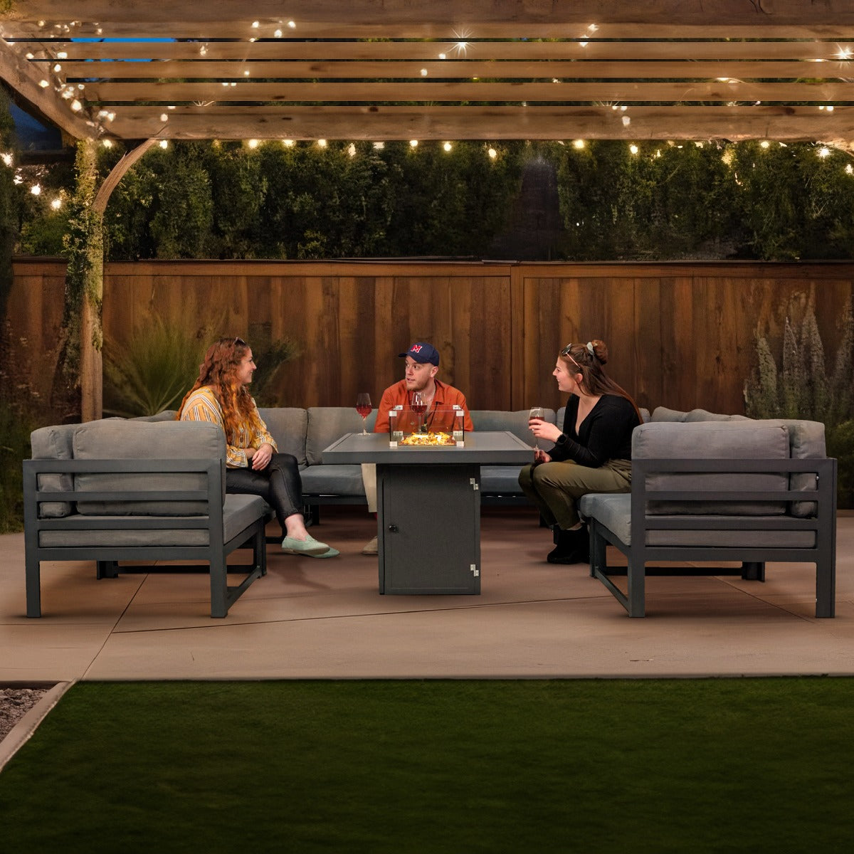 Modulares Gartenlounge-Set mit grauen Kissen und integrierter Feuerstelle, umgeben von einer gemütlichen Terrasse und stimmungsvoller Beleuchtung