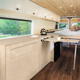 Moderne Küchenzeile im Wohnmobil mit hellem Holz, eleganter Arbeitsplatte, integrierter Spüle, Kühlschrank und gemütlichem Essbereich, umgeben von Fenstern