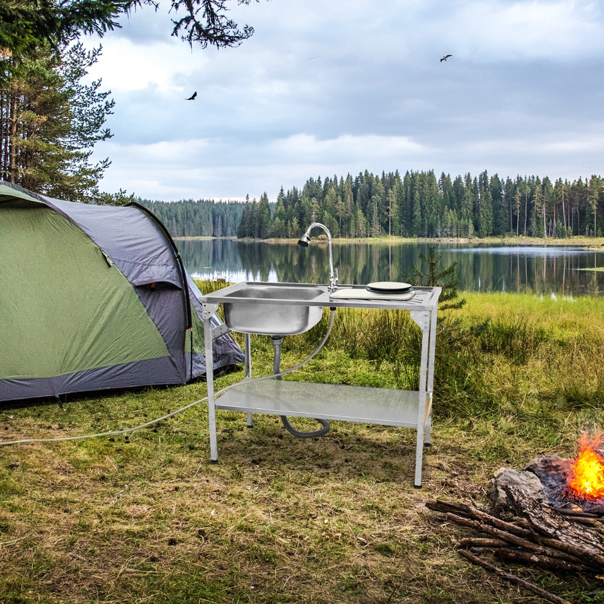 Faltbarer Camping-Spültisch in Weiß mit Edelstahlbecken, auf Rasen vor einem Zelt, umgeben von Wald und einem ruhigen See, ideal für Outdoor-Aktivitäten