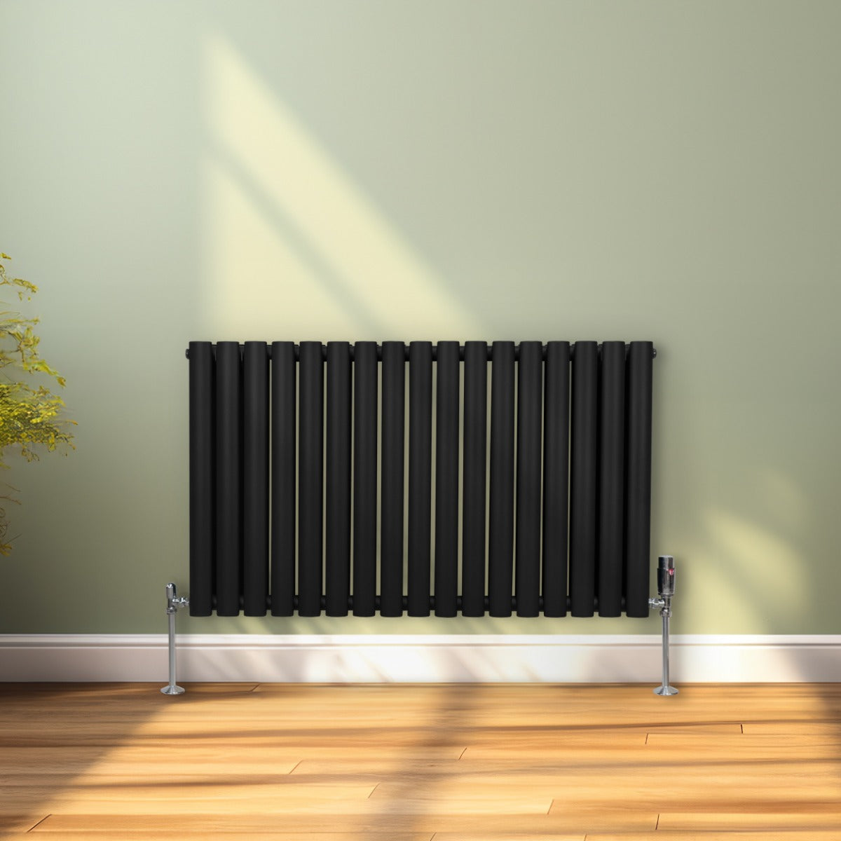 Ovaler Röhrenheizkörper in Schwarz, 600mm x 1020mm, mit vertikalen Röhren und glänzenden Ventilen, vor einer hellgrünen Wand auf einem Holzboden