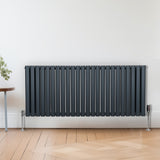 Ovaler Röhrenheizkörper in Anthrazitgrau, 600mm x 1440mm, mit vertikalen Lamellen und glänzender Oberfläche, elegant an einer hellen Wand montiert