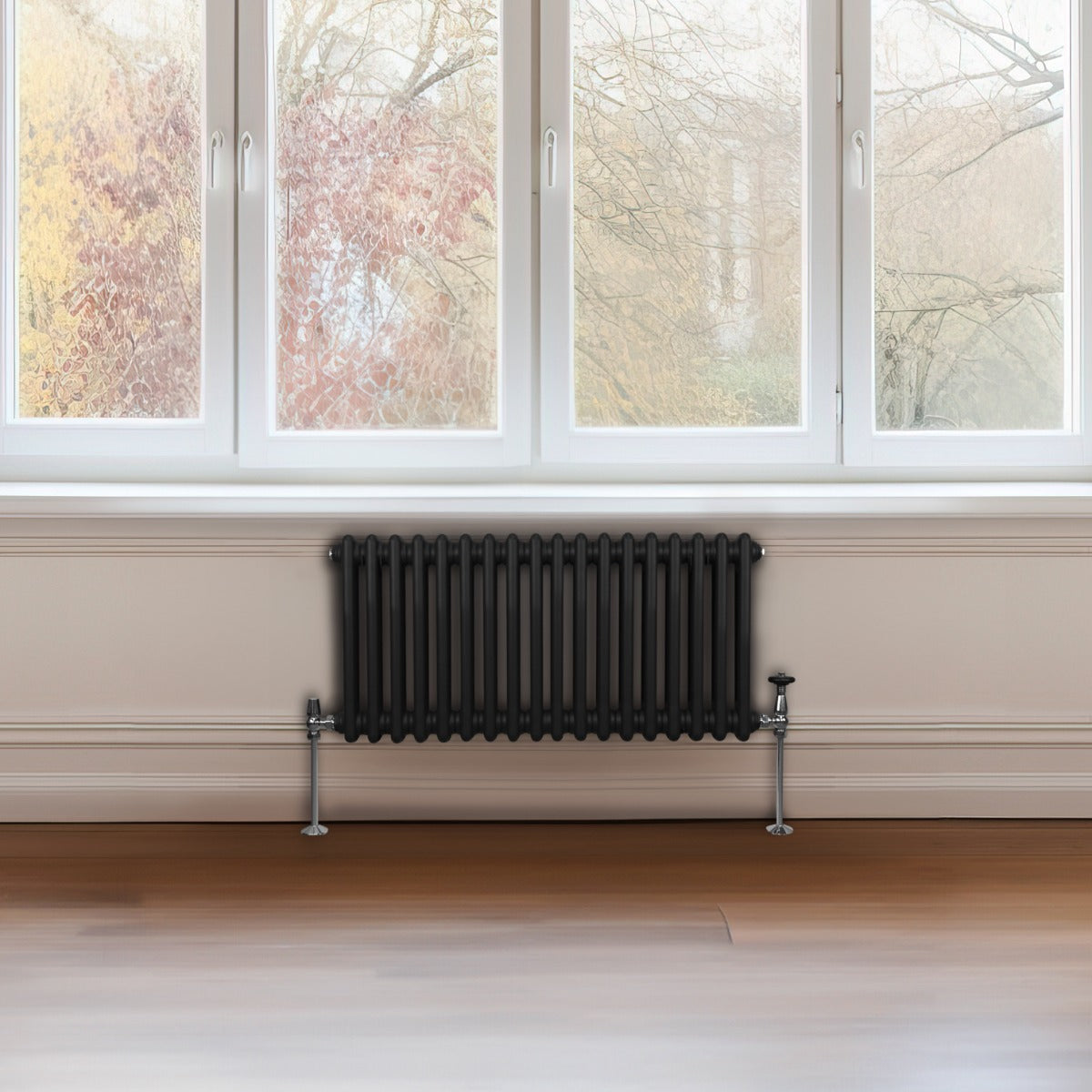Traditioneller 2-Spalten-Heizkörper in Schwarz, 300 x 832 mm, mit glänzenden Metallfüßen, vor einem großen Fenster mit natürlichem Licht