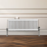 Traditioneller 2-Spalten-Heizkörper in Weiß, 300 x 1012 mm, mit geripptem Design und verchromten Füßen, vor einer hellen Wand und Holzfußboden