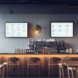 Zwei LED-Leuchtrahmen im DIN A2-Format an einer grauen Wand, präsentieren ein Menü in klarer Schrift, umgeben von einem modernen Café-Ambiente