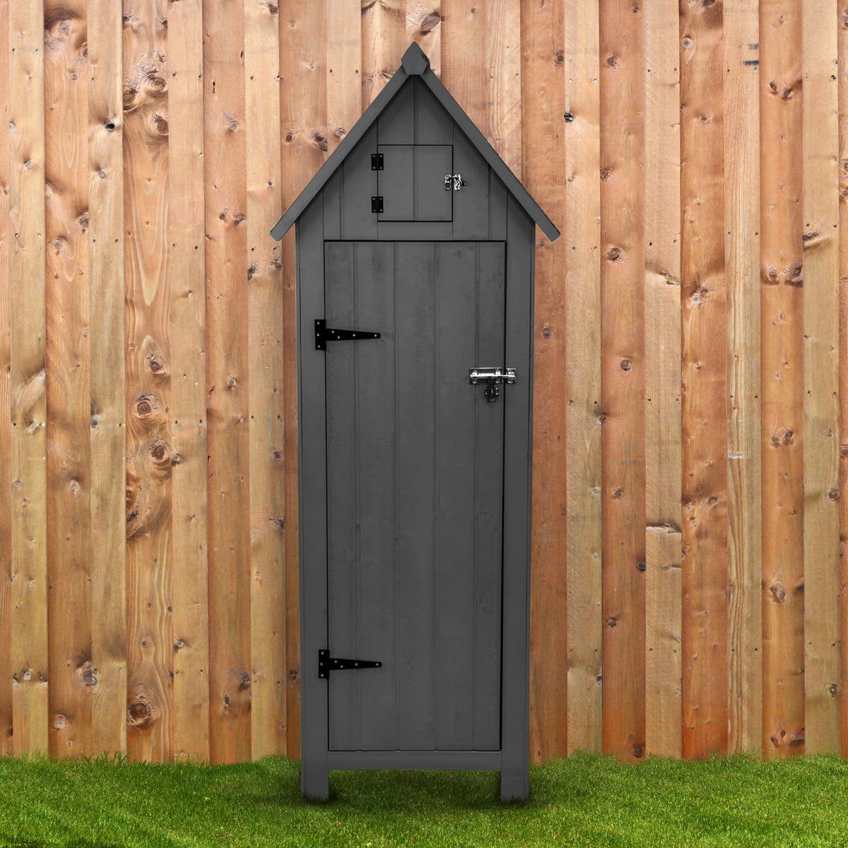 Grau lackierter Gartenschrank aus Holz mit spitzem Dach, stabilen Scharnieren und einem kleinen oberen Fach, vor einer Holzlattenwand platziert