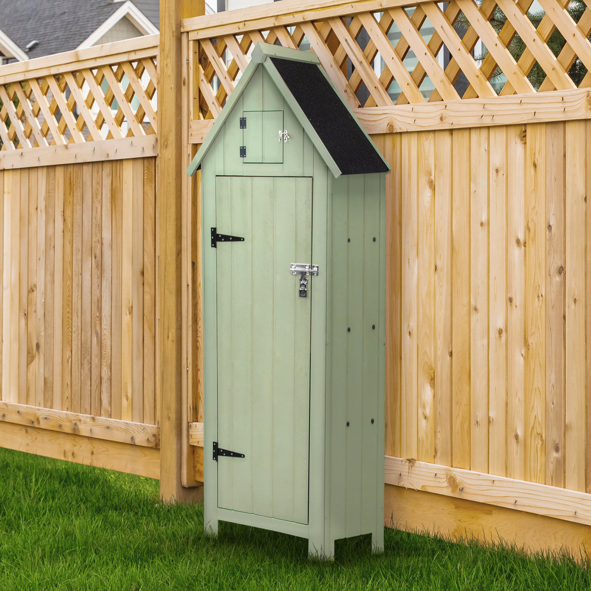 Holz-Gartenschrank in sanftem Grün mit schwarzem Dach, verziert mit einem kleinen Fenster und stabilen Metallbeschlägen, vor einem Holzzaun platziert