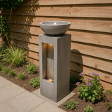 Elegante elektrische Wasseranlage "Serenity Falls" aus grauem Beton mit sanft fließendem Wasser und einer dekorativen Schale oben, umgeben von grünen Pflanzen