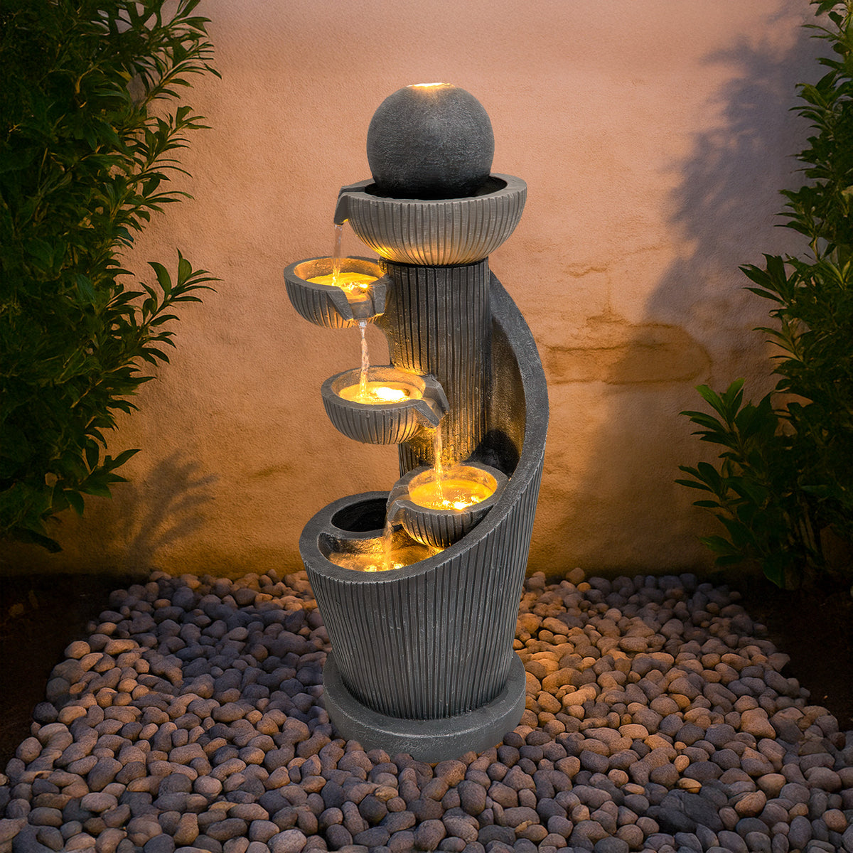 Elegante elektrische Wasseranlage "Spiral Springs" aus grauem Stein mit sanft fließendem Wasser, beleuchtet von warmen Lichtern, umgeben von Kieselsteinen
