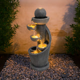 Elegante elektrische Wasseranlage "Spiral Springs" aus grauem Stein mit sanft fließendem Wasser, beleuchtet von warmen Lichtern, umgeben von Kieselsteinen